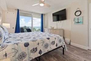 Une chambre à coucher avec un lit, un ventilateur de plafond, une télévision, une fenêtre avec des rideaux et une vue sur l’extérieur.