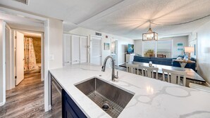 Een moderne keuken met een groot kookeiland, een inbouwgootsteen en een eethoek met een blauwe bank en een kroonluchter.