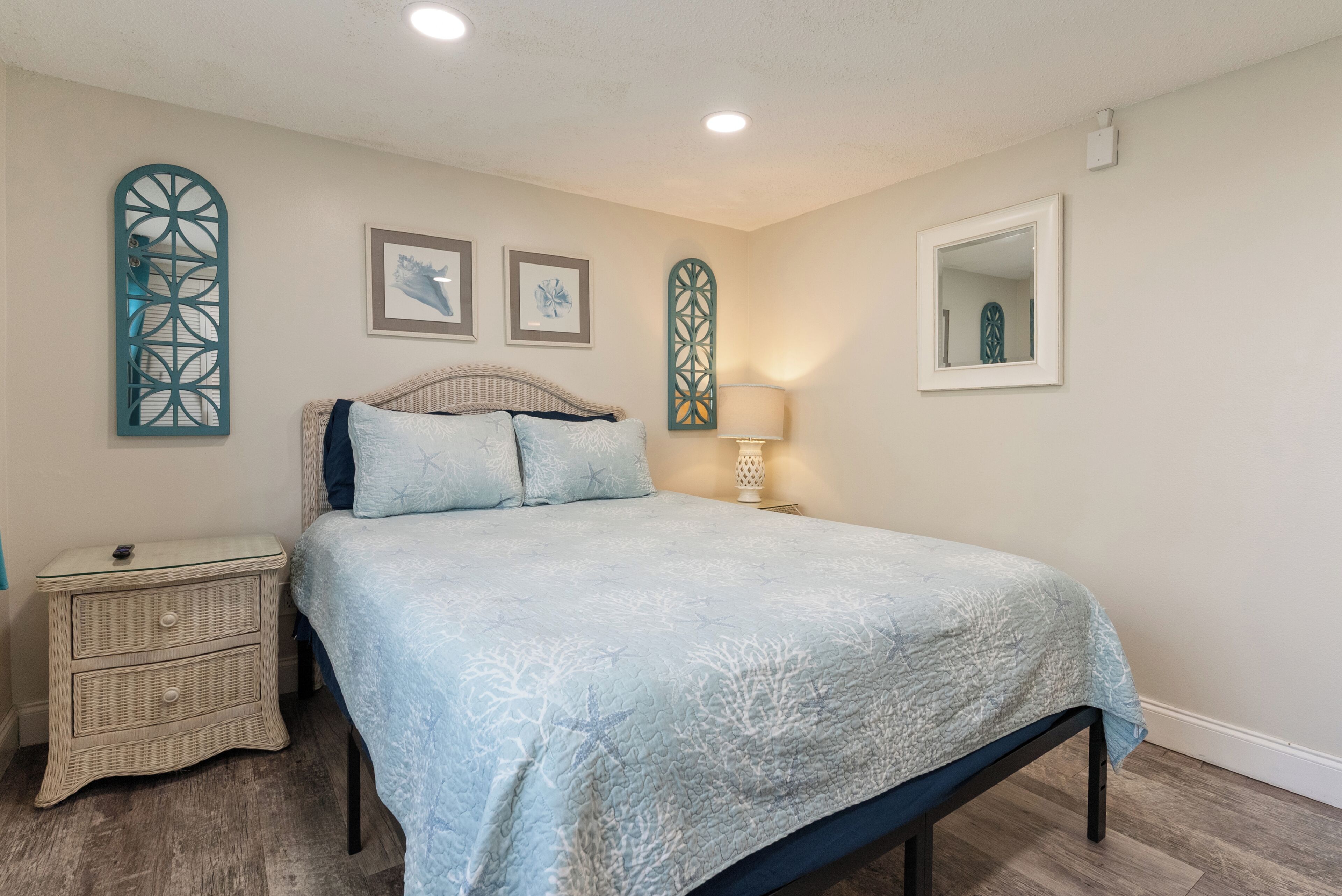 A bedroom with a bed, nightstand, wall art, and a mirror.