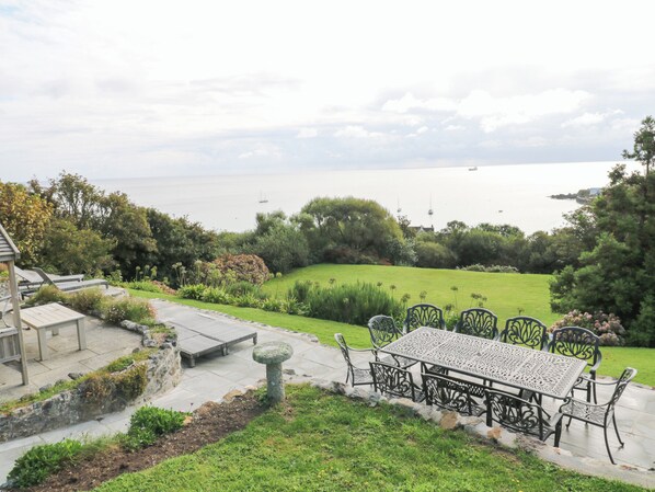 A patio with a table and chairs overlooking a grassy area and the sea.