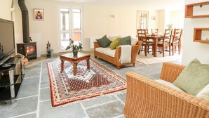 A cozy living room with a fireplace, a television, a dining area with wooden furniture, and a patterned rug. - The Hermitage (Holt)