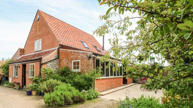 A traditional brick house with a sloped red-tiled roof, a small attached structure with a glass door, and a paved driveway. - The Hermitage (Holt)