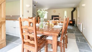 A dining area with a wooden table set for breakfast, a vase with flowers, and a fireplace in the background. - The Hermitage (Holt)