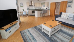 A modern living room with a flat-screen TV, a coffee table, and a sofa. - Apartment 6 (Pwllheli)