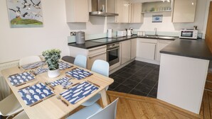A modern kitchen with a dining area, featuring a central island, stainless steel appliances, and light-colored cabinetry. - Apartment 6 (Pwllheli)