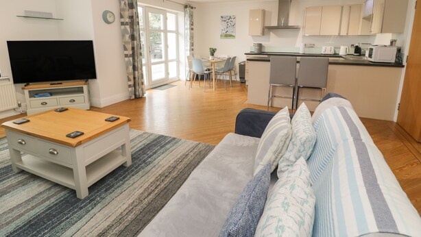 A modern living room with a sofa, coffee table, TV, and dining area. - Apartment 6 (Pwllheli)