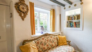 Et værelse med en blomstret sofa, en reol, et vindue med gardiner og et dekorativt vægur.