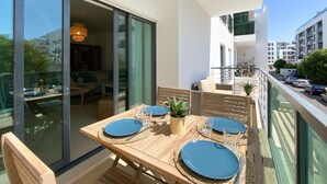Un balcón con una mesa dispuesta para cuatro, una planta en maceta y vistas a la calle y otros edificios.
