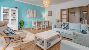 Una sala de estar con una pared azul claro, un mueble blanco, una mesa de comedor con sillas, un sofá y una lámpara colgante.