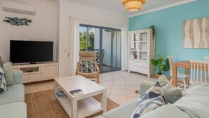 Una sala de estar con televisor, sofá, mesa de centro y un comedor con sillas y mesa.