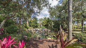 A landscaped garden with a pond, palm trees, and various shrubs. - Luxury 3BR Caribbean Retreat nr Disney (Davenport)