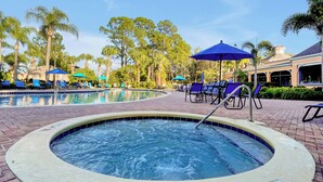 A pool area with lounge chairs and umbrellas, surrounded by palm trees and a building in the background. - Luxury 3BR Caribbean Retreat nr Disney (Davenport)