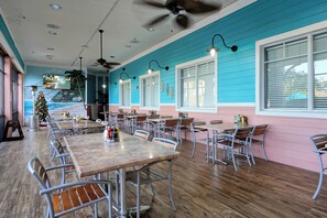Un vaste espace dédié à la salle à manger, avec de nombreuses tables et chaises, des ventilateurs de plafond et de grandes fenêtres.