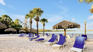 A beach with white lounge chairs and thatched umbrellas, palm trees, and a view of the water. - Luxury 3BR Caribbean Retreat nr Disney (Davenport)