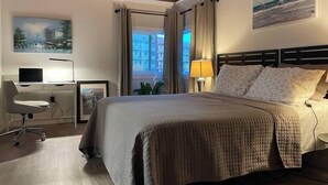 Ein modernes Hotelzimmer mit einem großen Bett, einem Schreibtisch mit einem Laptop, einem Sessel und einem Bild an der Wand.