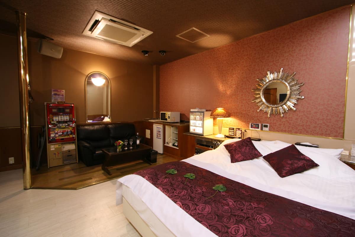 A hotel room with a bed, a desk, a chair, a mirror, and a minibar.
