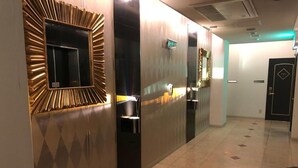 Un pasillo de diseño moderno, con un muro espejado con diseño geométrico, una puerta con placa de número y un suelo de baldosas.