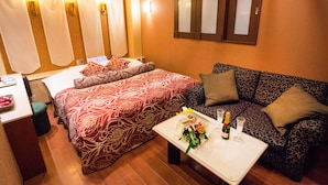 A hotel room with a large bed, a sofa, a small table with a bouquet of flowers and a bottle of champagne, and a mirror on the wall.