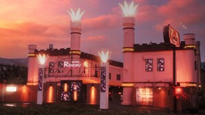 A hotel with a prominent entrance, two towers with illuminated tops, and a signboard displaying the hotel name.