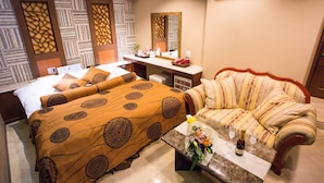 A hotel room with a bed, a sofa, a coffee table with a bottle and glasses, and a mirror.