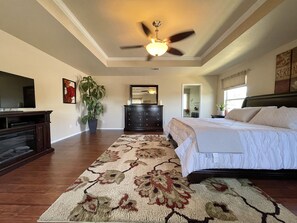 A bedroom with a bed, a dresser, a television, a ceiling fan, and a large potted plant.