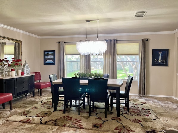 A dining room with a table and chairs, a chandelier, and a view of the outdoors through large windows.