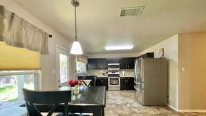 Una cocina moderna con armarios oscuros, electrodomésticos de acero inoxidable y un comedor con mesa y sillas.