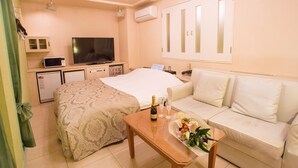 A hotel room with a bed, a sofa, a small table with a bottle and glasses, a television, a mini-fridge, and a microwave. - Restay SaKuRa - Adults Only (Hakodate)