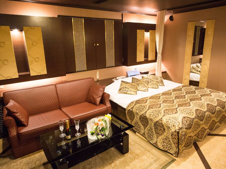 Quarto de hotel com cama, sofá, mesa de centro com uma garrafa e um copo, e um espelho.