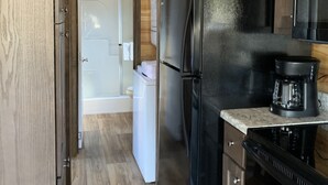 A compact kitchen with wooden cabinets, a black refrigerator, a coffee maker, and a white washing machine. - Tiny Homes for Rent, minutes to the Casino, Golf Course & Water Park.
 (Philadelphia)