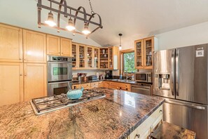 Eine moderne Küche mit Granit-Arbeitsplatten, Edelstahlgeräten, Holzschränken und einem eingebauten Backofen.