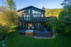 A modern two-story house with a deck, outdoor seating, and a hot tub.