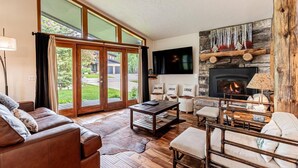 A spacious living room with a fireplace, leather sofa, and a large window overlooking a garden.