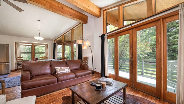 A spacious living room with a leather sofa, wooden coffee table, and large windows offering a view of the outdoors.
