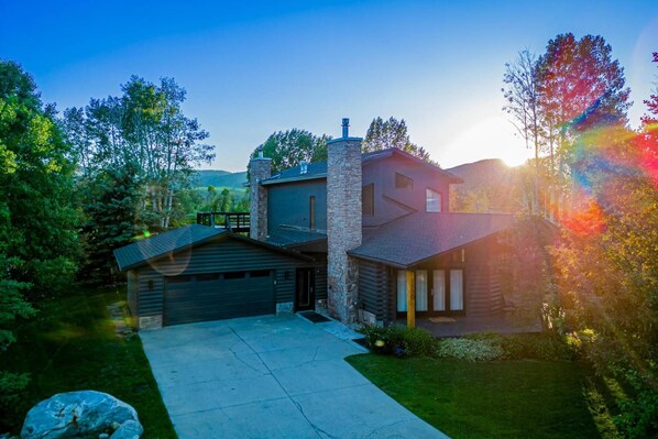 A modern log cabin with a stone chimney, a garage, and a well-maintained lawn.