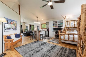 A modern living space with a wooden bench, a dining area, a kitchen, and a unique tree stump bed.