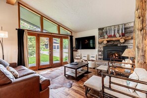 A spacious living room with a fireplace, a large window, and a stone wall.