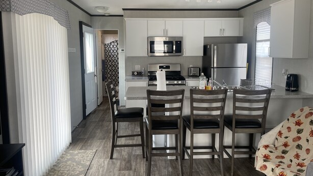 A compact kitchen with white cabinets, a microwave, a stove, and a refrigerator. There are four wooden chairs around a small table. -  Niagara-on-the-Lake Cottage (Niagara-on-the-Lake)