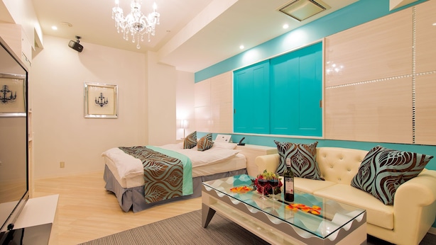 A modern hotel room with a glass coffee table, a sofa, a bed with a patterned bedspread, and a chandelier. - Restay Koriyama - Adults Only (Koriyama)