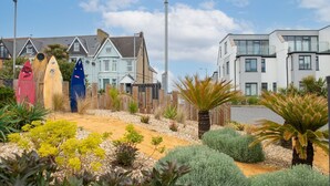 Zona residencial costera con casas, un jardín de arena y tablas de surf.