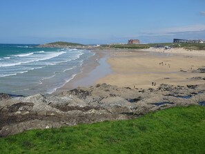 Ein Küstenstrand mit felsigem Vordergrund, einem Sandufer und Gebäuden im Hintergrund.