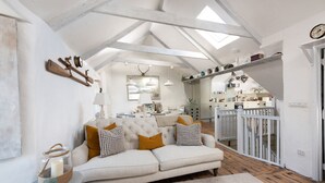 A cozy living room with a sofa, a small table with a candle, and a view into the kitchen. - Carvossa - Sea Views & Woodburner (Marazion)