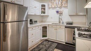 A modern kitchen with white cabinetry, stainless steel appliances, and a patterned rug. - Cozy 1-2 BR APT w/fireplace & Patio/Deck (Chicago)