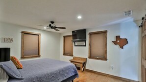 A bedroom with a bed, a ceiling fan, a TV, and a wooden bench. - B-Well Rafter J Lodge: A Family Gathering Place (Abilene)