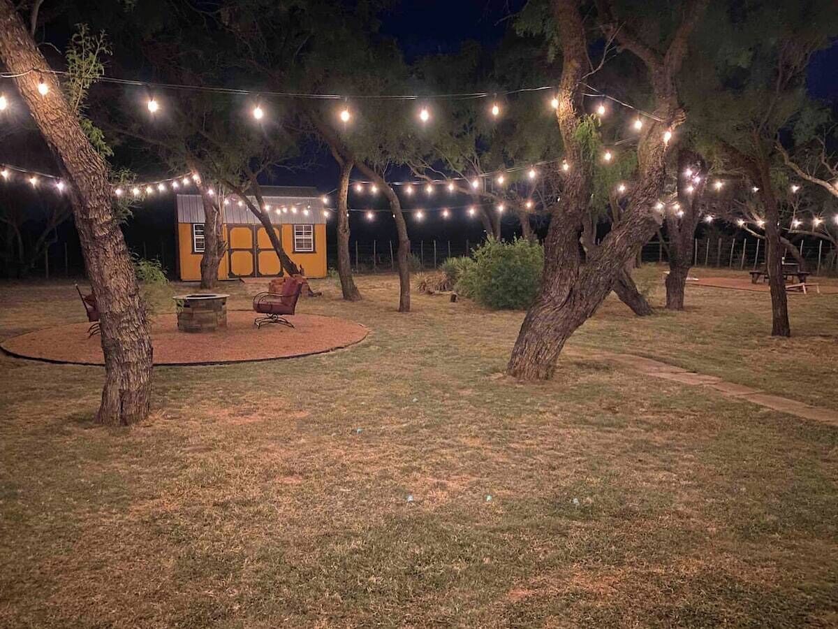 An outdoor area with string lights, a small building, and a fire pit.