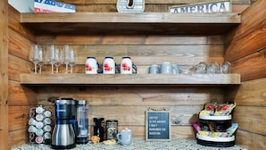 A wooden bar area with shelves holding glasses, mugs, and a coffee station.