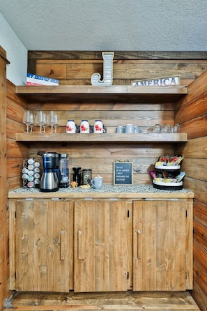 Una zona de bar con madera, con estantes que sostienen vasos, tazas y una estación de café.