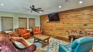A cozy living room with a sofa, chairs, a coffee table, a foosball table, and a ceiling fan.