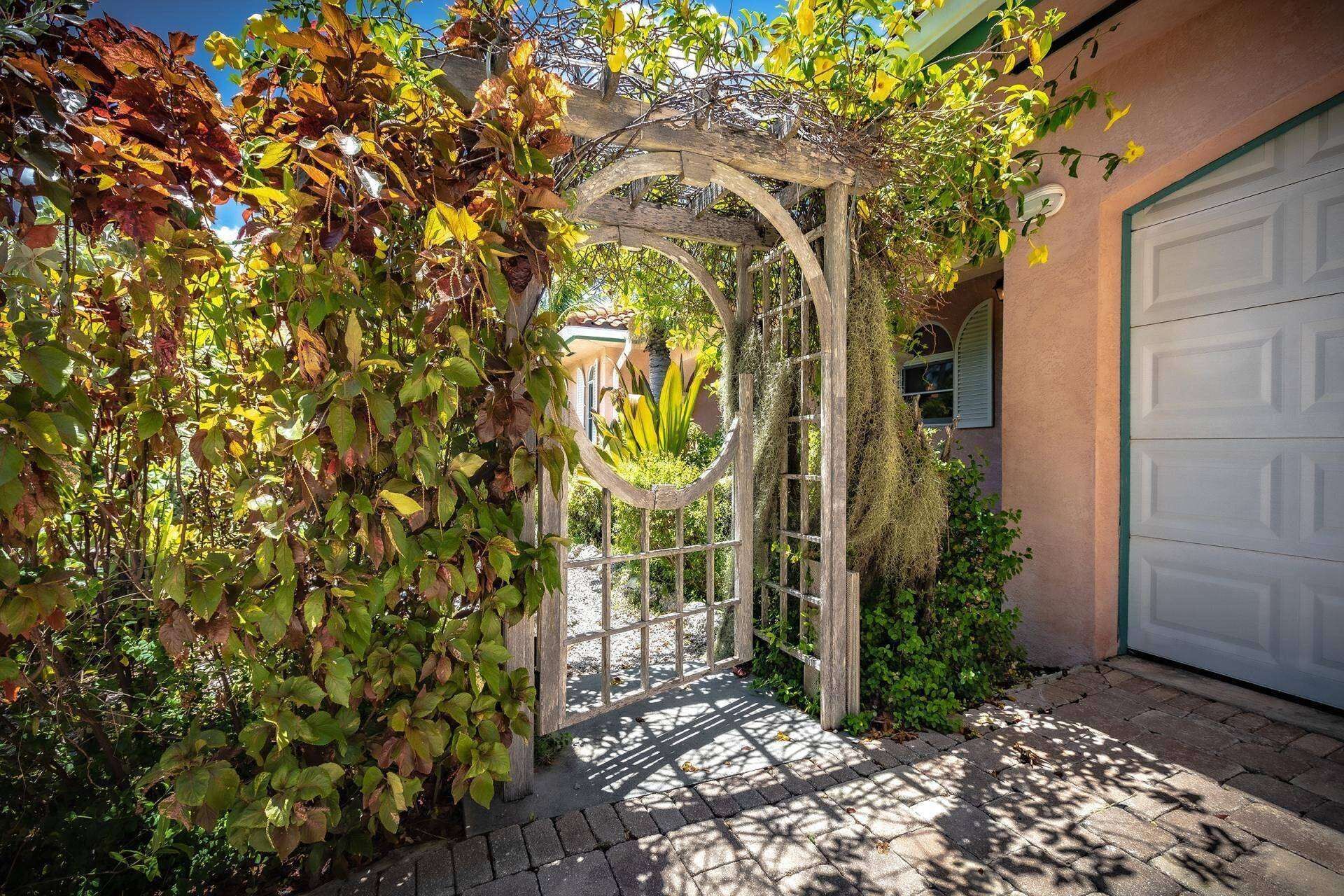 A wooden arbor with climbing plants, a paved walkway, and a garage door.