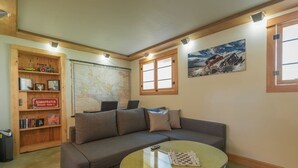 En stue med sofa, sofabord, reol, et kort og et maleri.